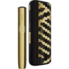 Gold IQOS tobacco heating device shown beside a black-and-gold patterned protective case, highlighting a premium minimalist design.